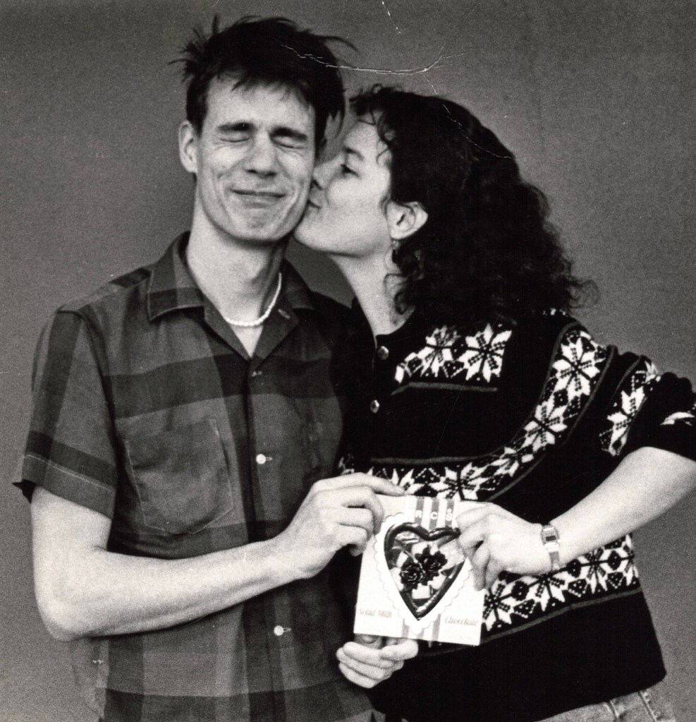 A young woman kissing a young man. They are holding a Valentine heart of 
chocolate.
